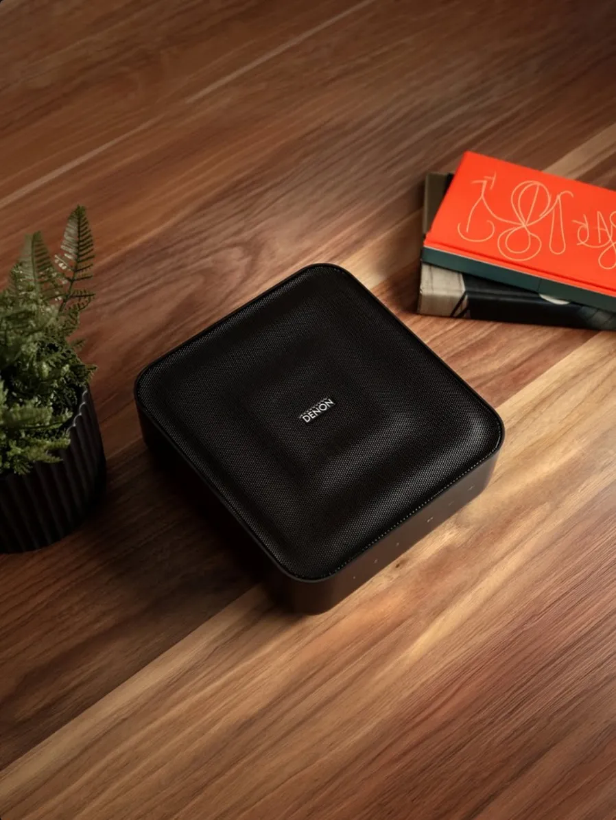 Denon Home Amp on a timber tabletop beside a plant and books