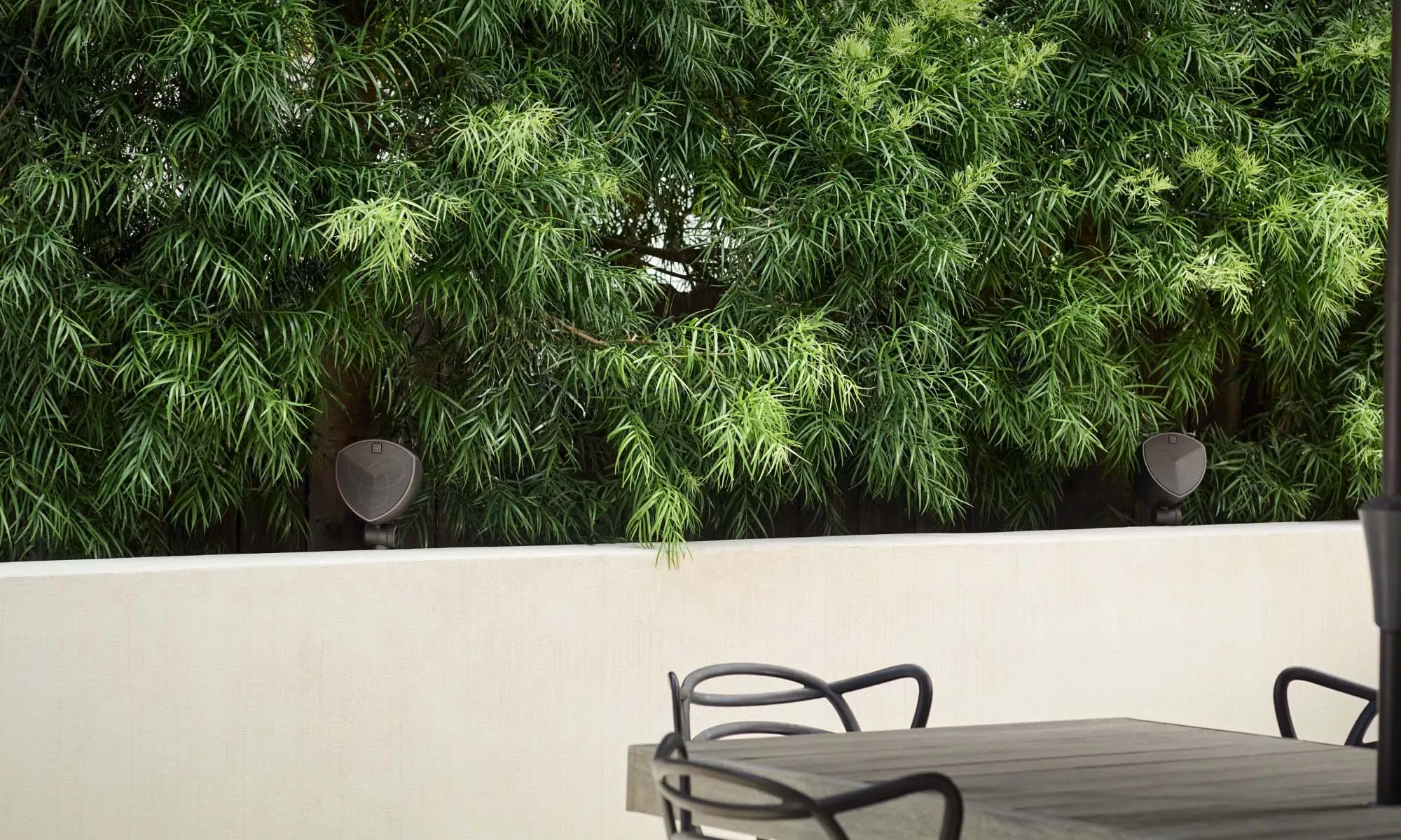 Outdoor dining area with an LS-400 speaker in the planting behind the table