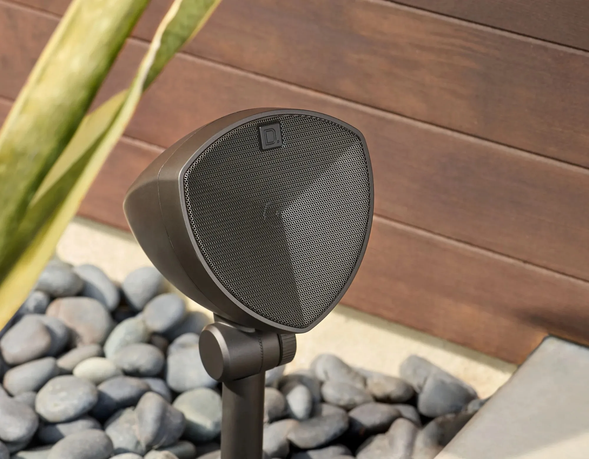 LS-400 landscape speaker in river pebbles in front of a timber wall